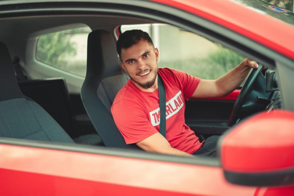 Smiling man driving a red car while wearing a seatbelt, showcasing safety and joy.