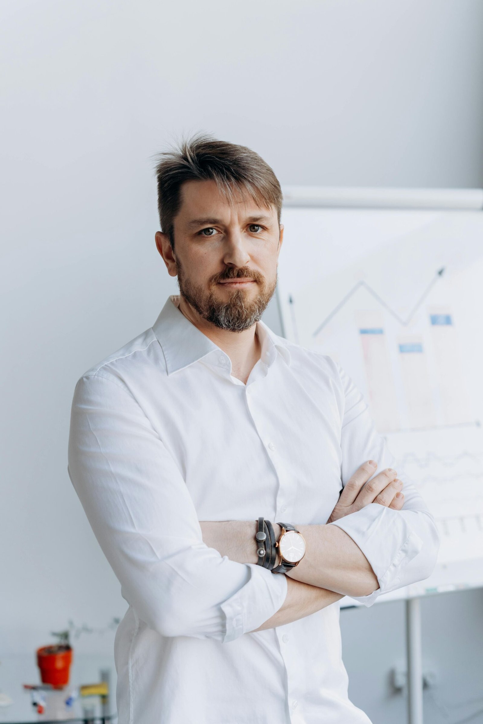 Confident businessman in white shirt posing in front of office chart.