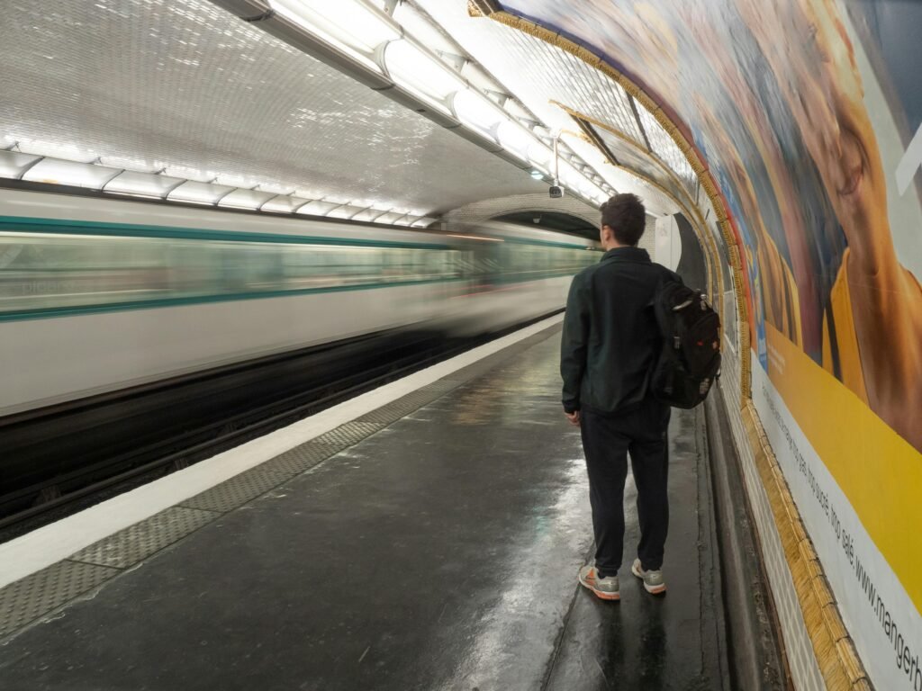 A person waits on a platform as a train speeds by in a Paris metro station.