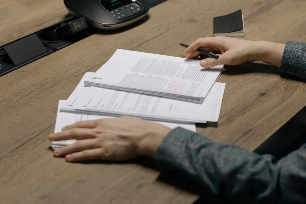 Comment regrouper ses contrats d'assurance pour payer moins cher à Arras ? Close-up of a person reviewing documents with a pen at a modern office desk.